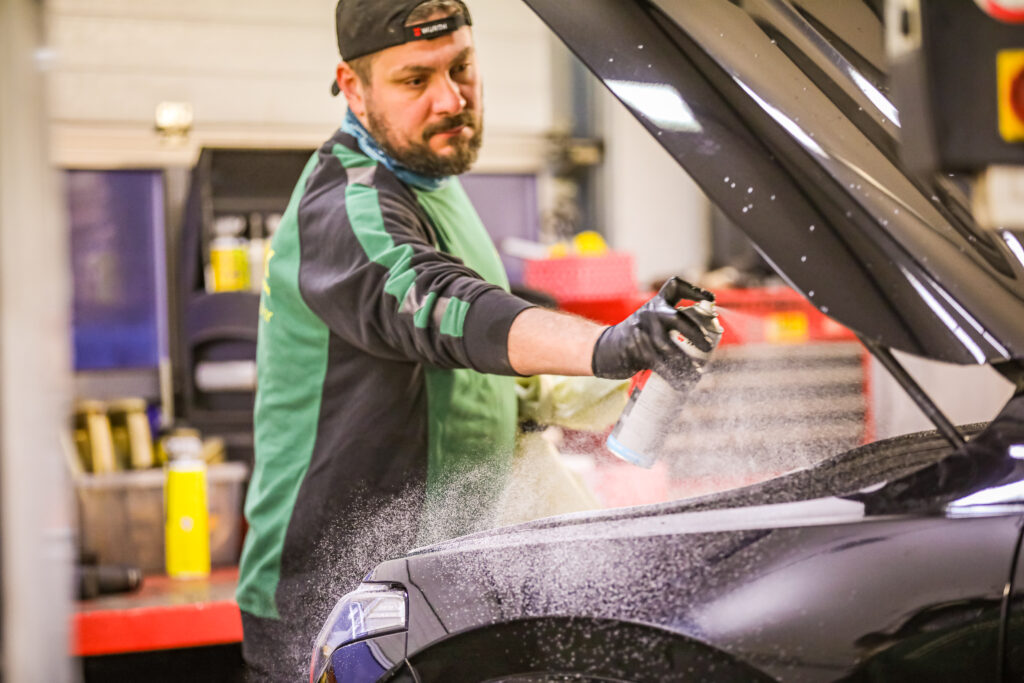 Bilde av Carfix-mekaniker som rengjører motoren på en bil. Han sprayer et rengjøringsmiddel over motoren.