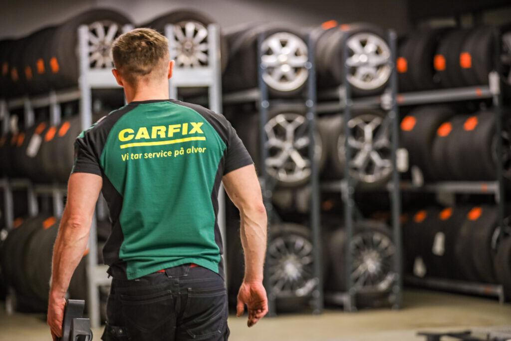Bilde av ryggen til Carfix-mekaniker som er på vei bort til dekkhotellet. I bakgrunnen er det mange hjul i hyller.