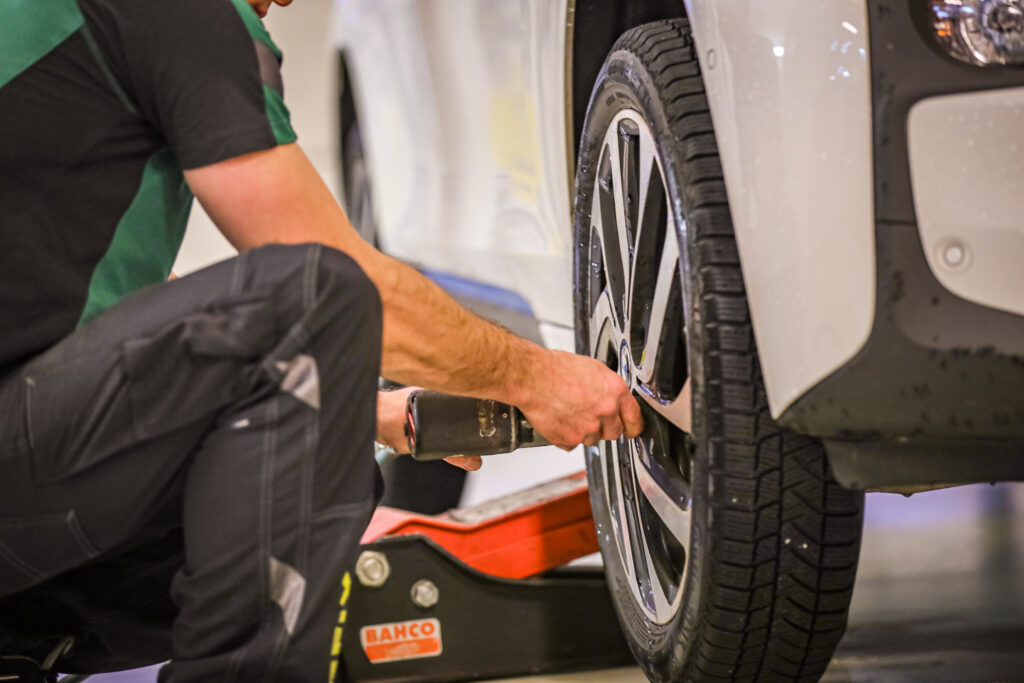 Bilde av Carfix-mekaniker som holder på å feste et hjul til en bil. Bilen står nesten helt nede på gulvet, og mekanikeren står på huk.