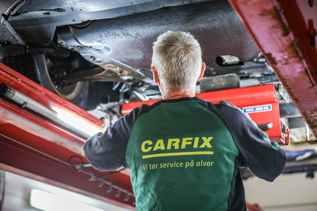 Bilde av ryggen til en Carfix-mekaniker som sjekker understellet til en bil på løftebukk.