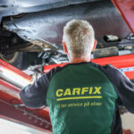 Bilde av ryggen til en Carfix-mekaniker som sjekker understellet til en bil på løftebukk.