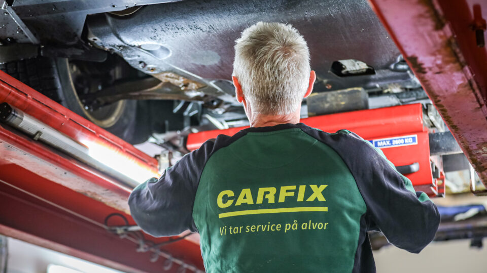 Bilde av ryggen til en Carfix-mekaniker som sjekker understellet til en bil på løftebukk.