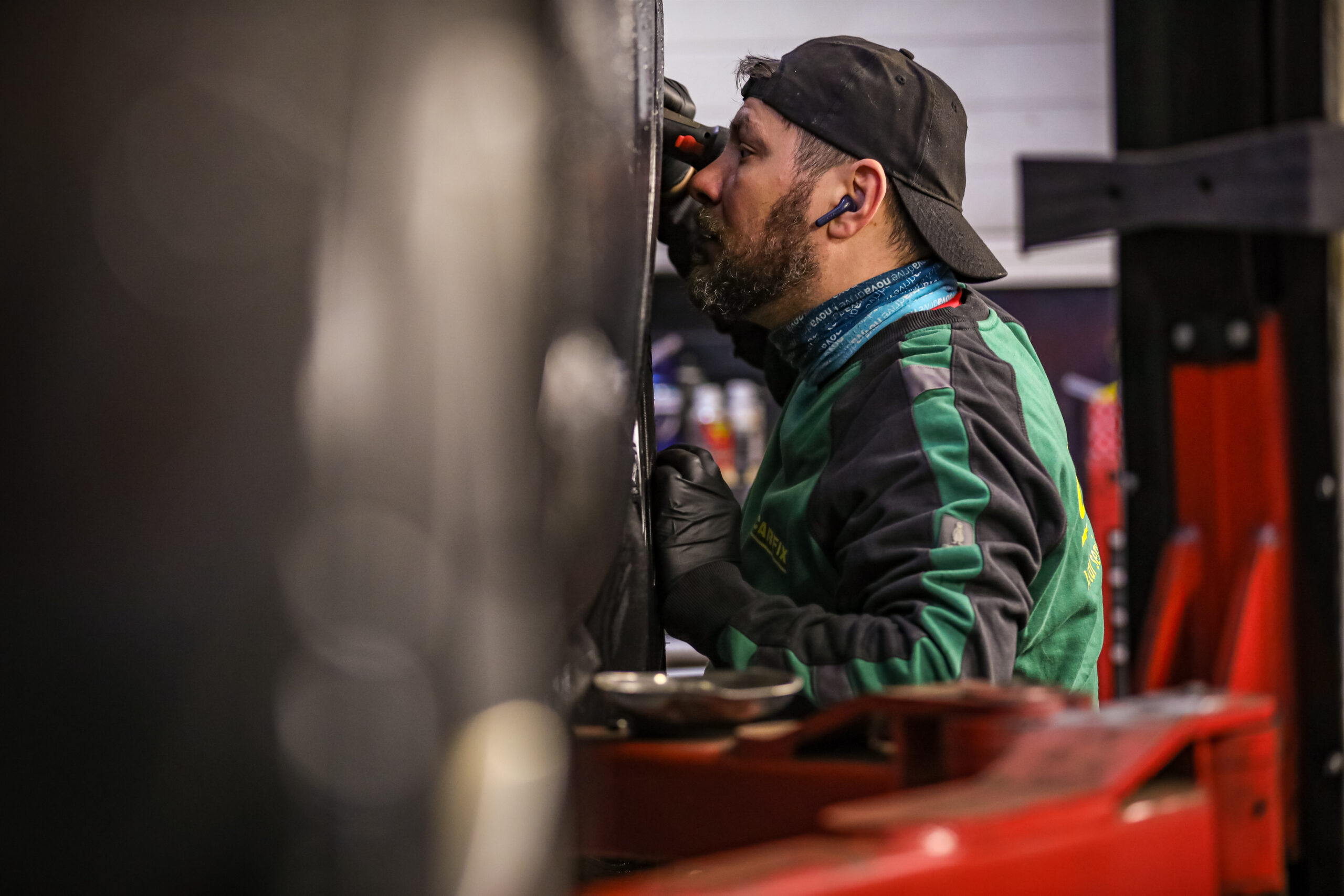 Bilde av Carfix-mekaniker som lyser oppunder hjulbuen på en bil som henger på bukk inne på et bilverksted.