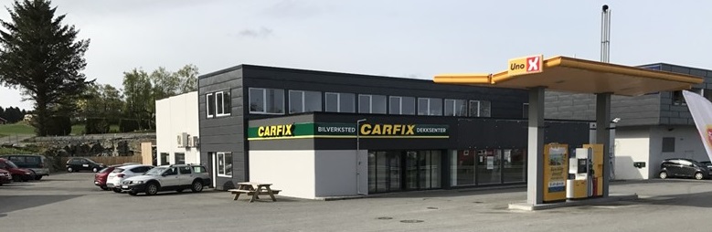 Bilde av utsiden av Carfix Fitjar med Carfix-profilering. Det er parkeringsplasser på venstre siden av bygget, der står det også en benk. Bensinstasjonen Uno-x er vegg-i-vegg.