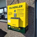 Bilde av automatisk nøkkelautomat som henger på murvegg utenfor et Carfix-verksted. Boksen er gul, og det står "bilnøkler" med stor skrift øverst på boksen. Vi har nøkkeldropp!